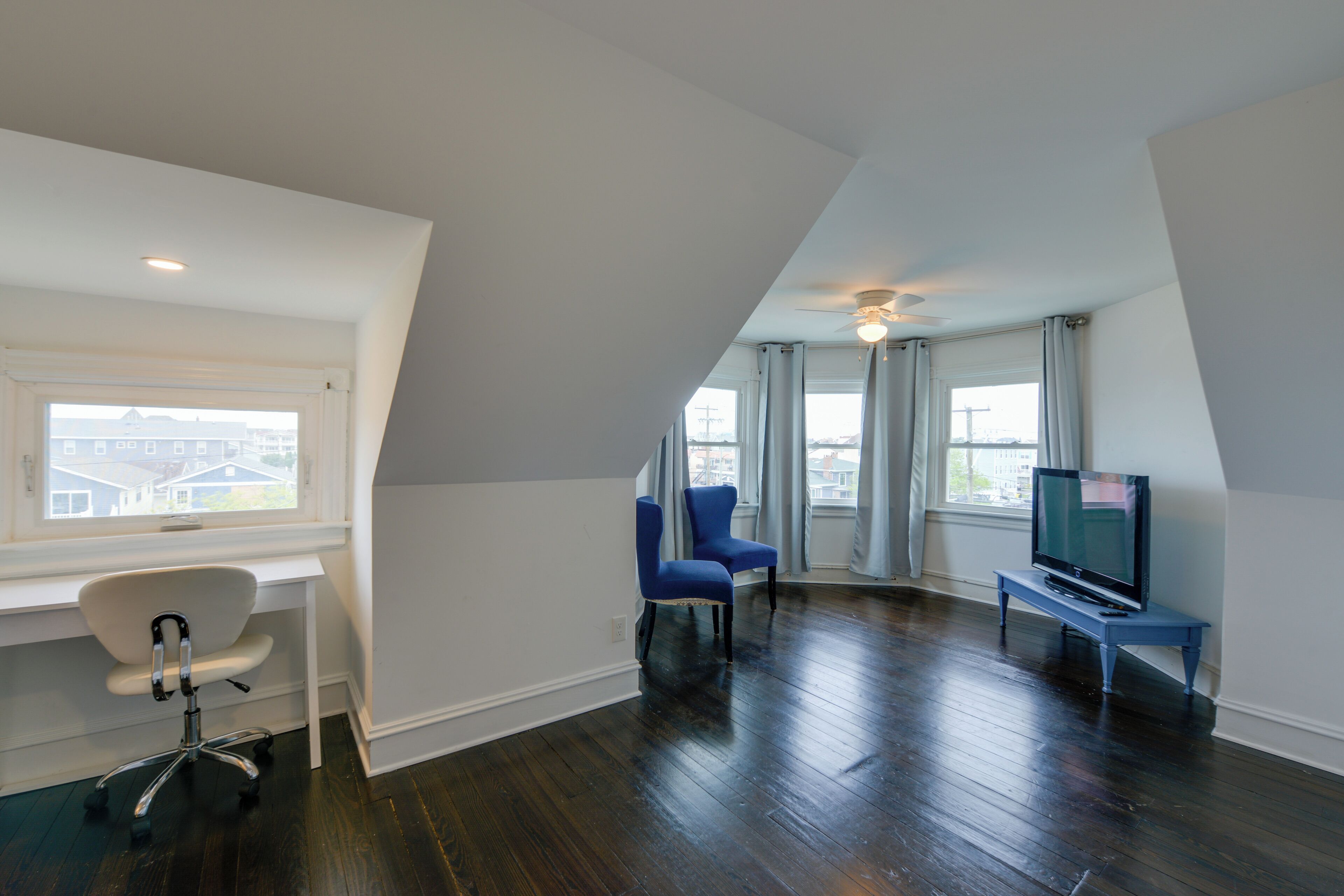 A room with a desk, two chairs, a television on a stand, and a large window.