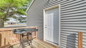 A wooden deck with a metal table, a white door, and a house with grey siding. - Cozy Lewiston Home - Near Lakes & Restaurants! (Lewiston)