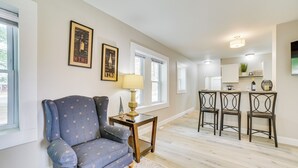 A living room with a blue armchair, a small table with a lamp, and a kitchen area with bar stools. - Cozy Lewiston Home - Near Lakes & Restaurants! (Lewiston)