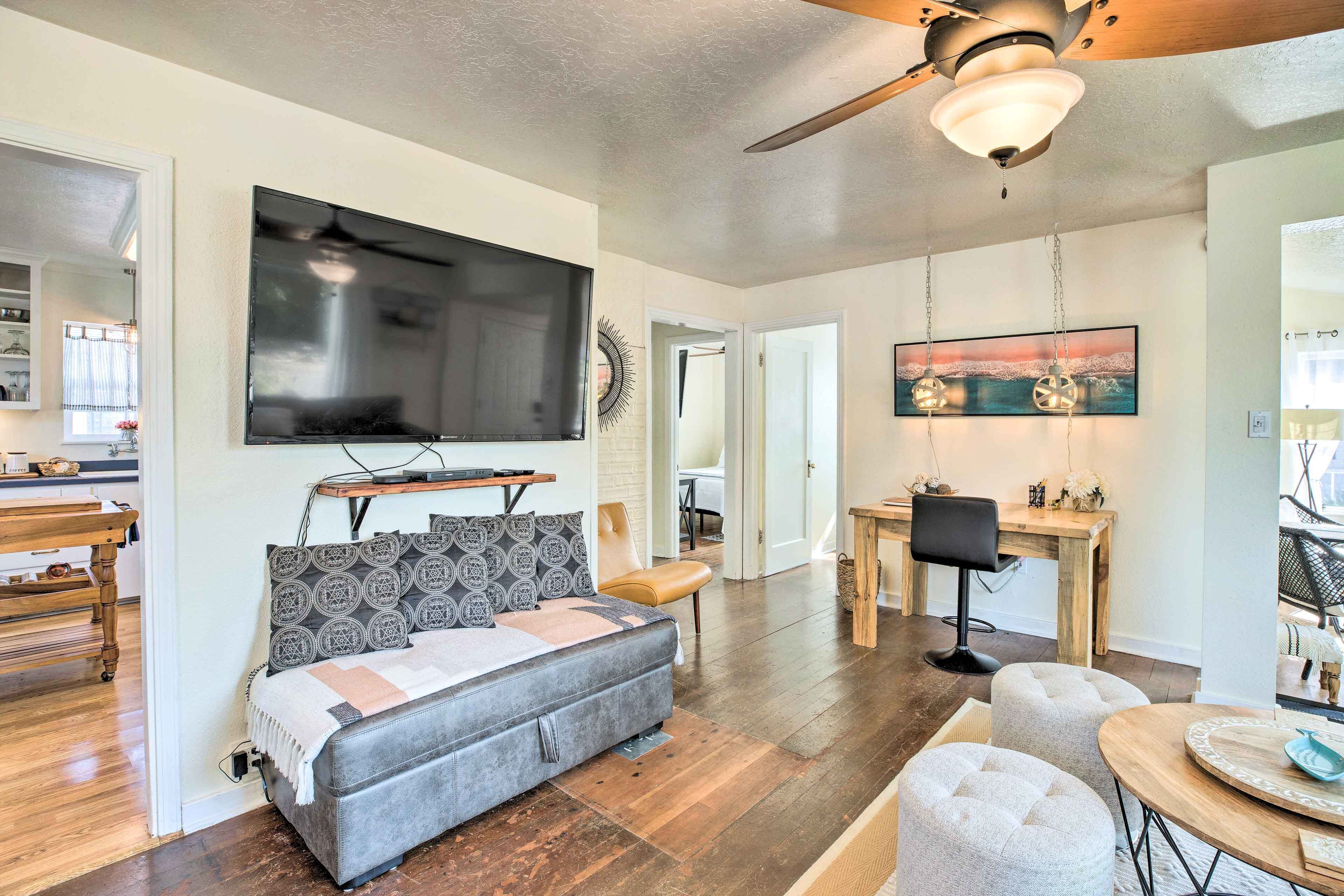 A modern living room with a flat-screen TV, a sofa, a dining area, and a ceiling fan.