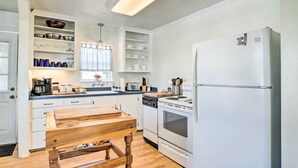 Eine Küche mit weißen Schränken, einem Holztisch, einem Kühlschrank und einem Geschirrspüler.