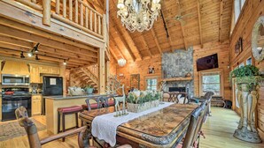 A wooden cabin interior with a dining area, kitchen, and a stone fireplace. - Walk to Golfing: Grand Maggie Valley Cabin! (Maggie Valley)