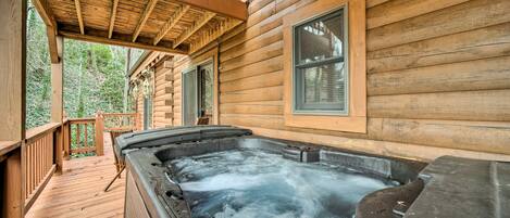A wooden cabin with a hot tub on a wooden deck, surrounded by trees.