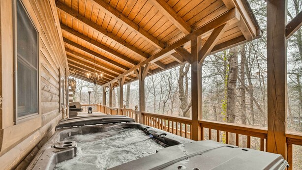 A wooden cabin with a hot tub on the porch, surrounded by trees. - Walk to Golfing: Grand Maggie Valley Cabin! (Maggie Valley)