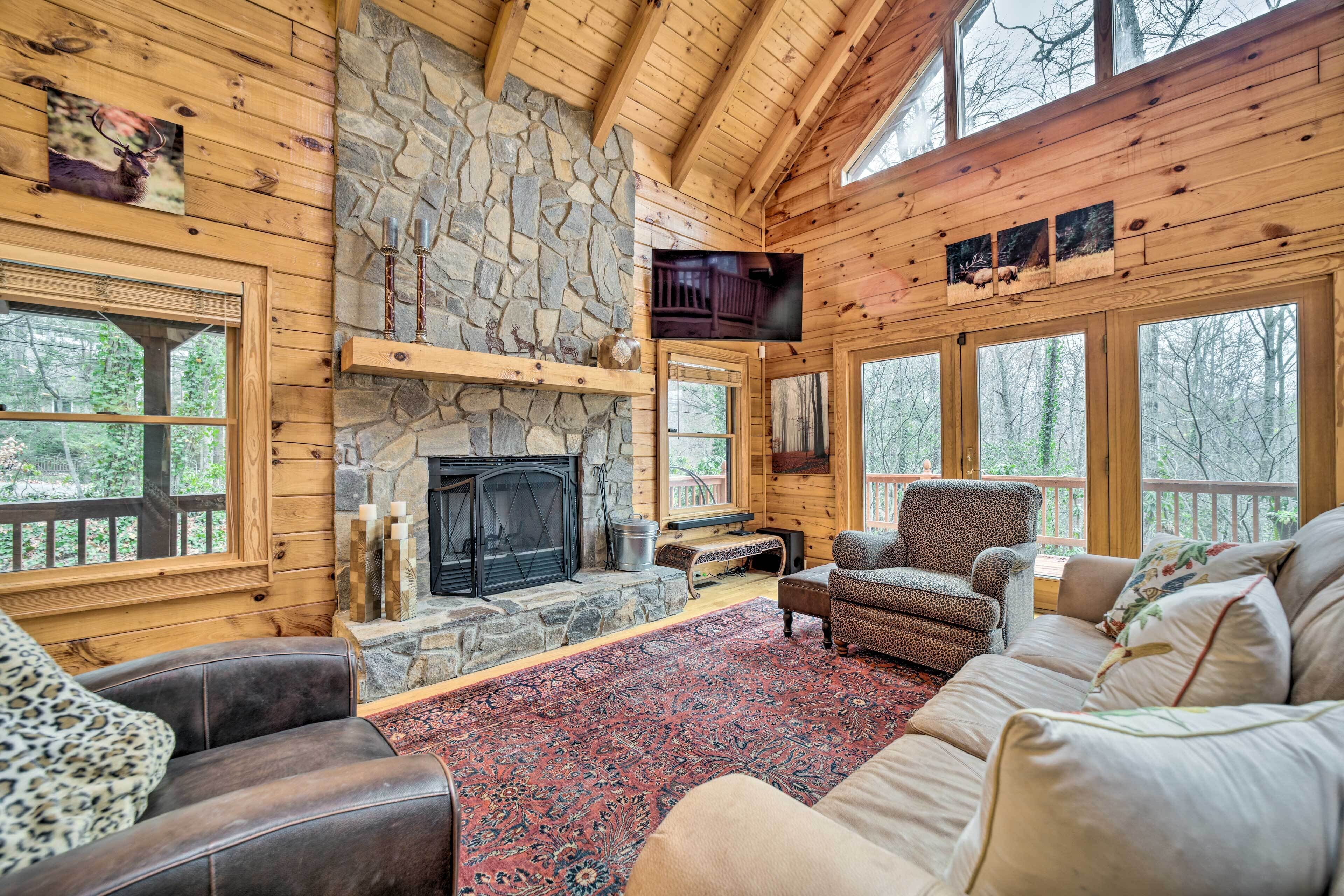 A cozy cabin interior with a stone fireplace, wooden walls, and large windows.