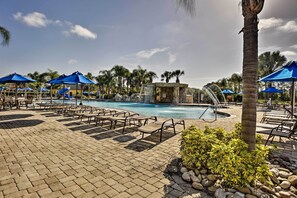 A pool area with lounge chairs, umbrellas, and a small waterfall feature. - Modern Kissimmee Townhome w/ Fenced Pool & Patio! (Kissimmee)