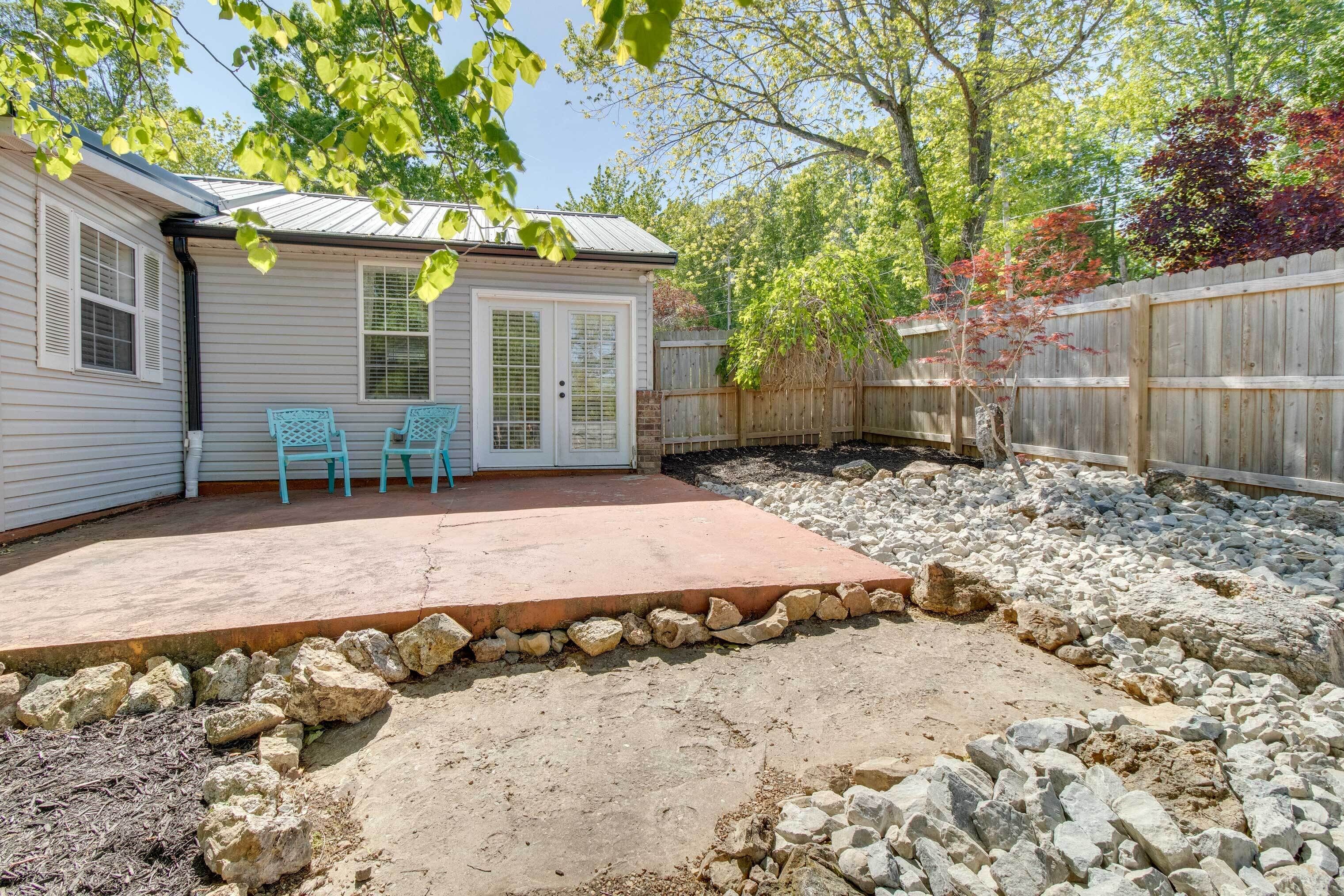 A backyard with a patio, two blue chairs, a wooden fence, and a house with white siding.