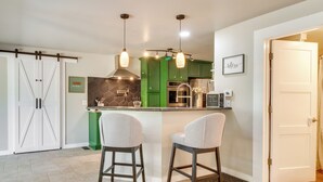 Een moderne keuken met groene kasten, een centraal eiland, twee barkrukken, hanglampen en een schuifdeur in boerderijstijl.