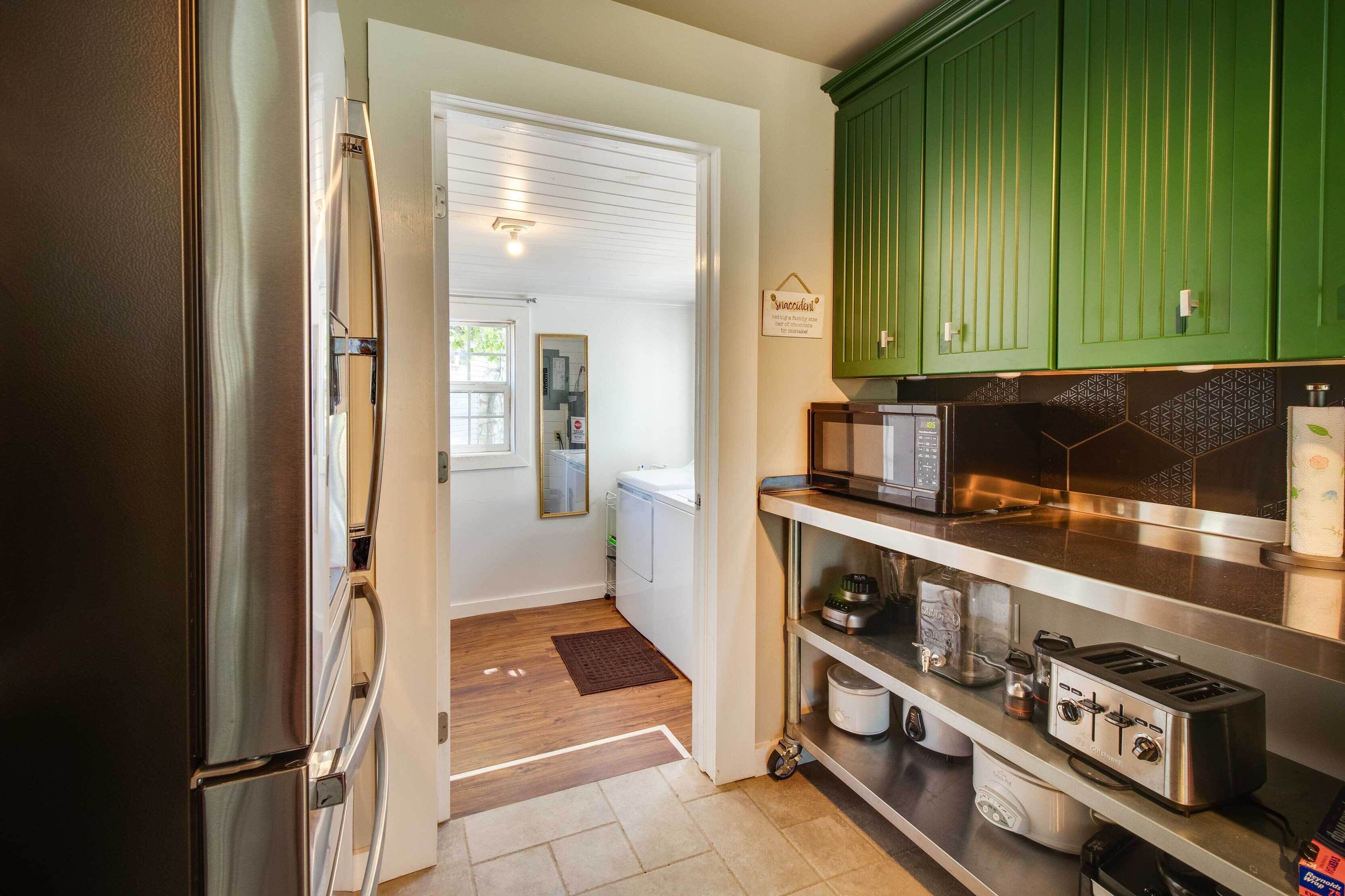A kitchen with a stainless steel refrigerator, a microwave, a toaster, and green cabinets.