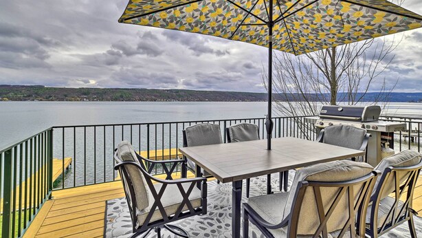 Eine Terrasse im Freien mit Tisch, Stühlen, einem Grill und Blick auf einen See.