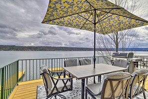 An outdoor deck with a table and chairs, a grill, and a view of a lake. - Charming Home on Keuka Lake w/ Dock & Fire Pit! (Hammondsport)