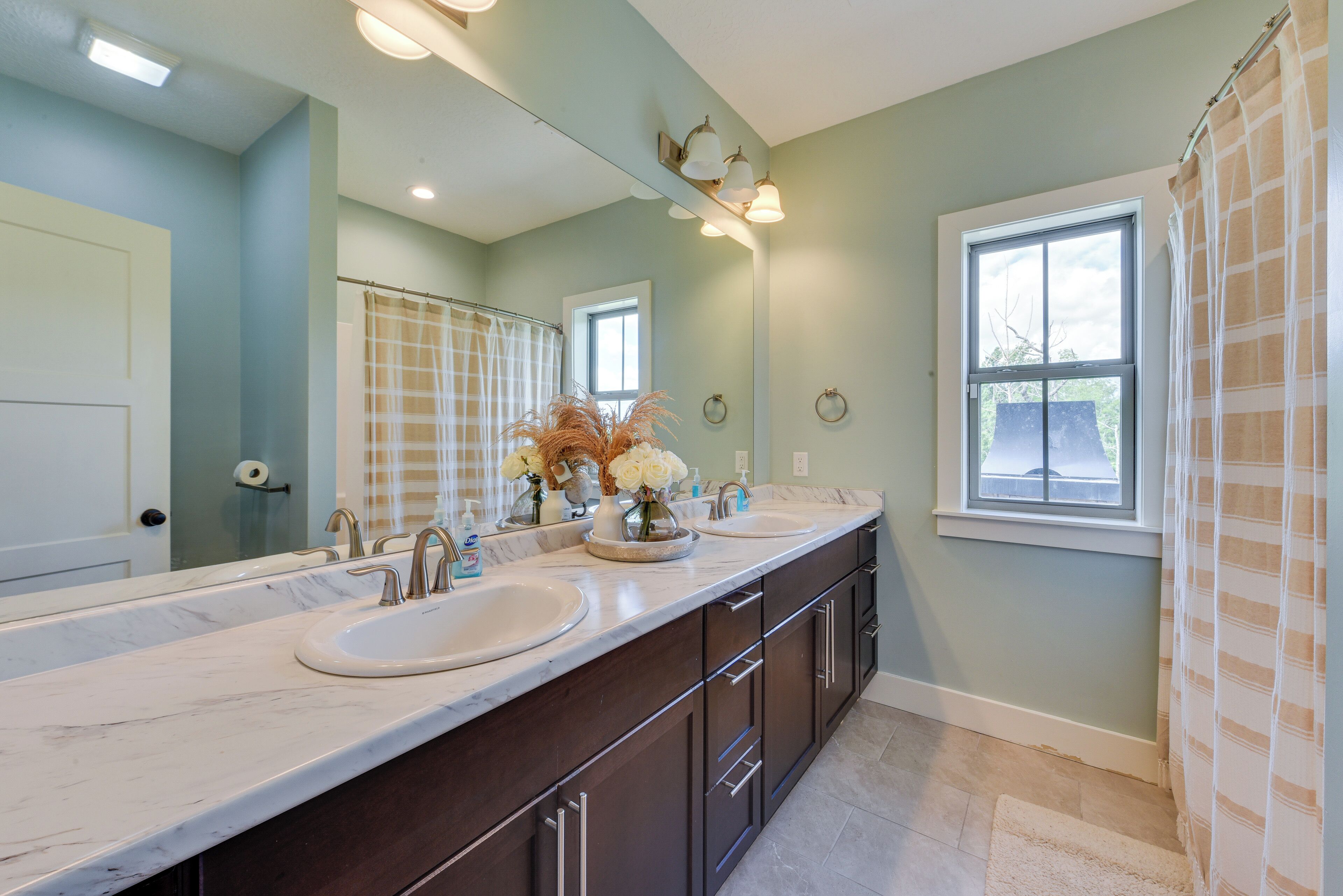 A bathroom with a double sink vanity, a large mirror, and a window with a view of the outside.