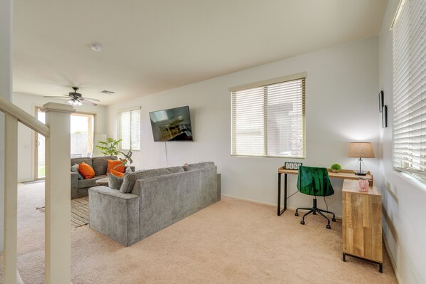A living room with a grey sectional sofa, a TV mounted on the wall, a wooden desk, and a chair.