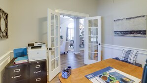 Een kamer met een houten eettafel, openslaande deuren naar een andere ruimte en een kunstwerk aan de muur.