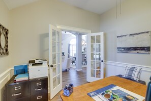 Um quarto com uma mesa de jantar de madeira, portas abertas que dão para outro espaço e uma obra de arte na parede.