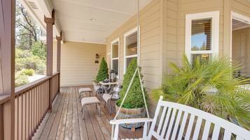 A wooden porch with a white bench, a hanging planter, and a small table with chairs.