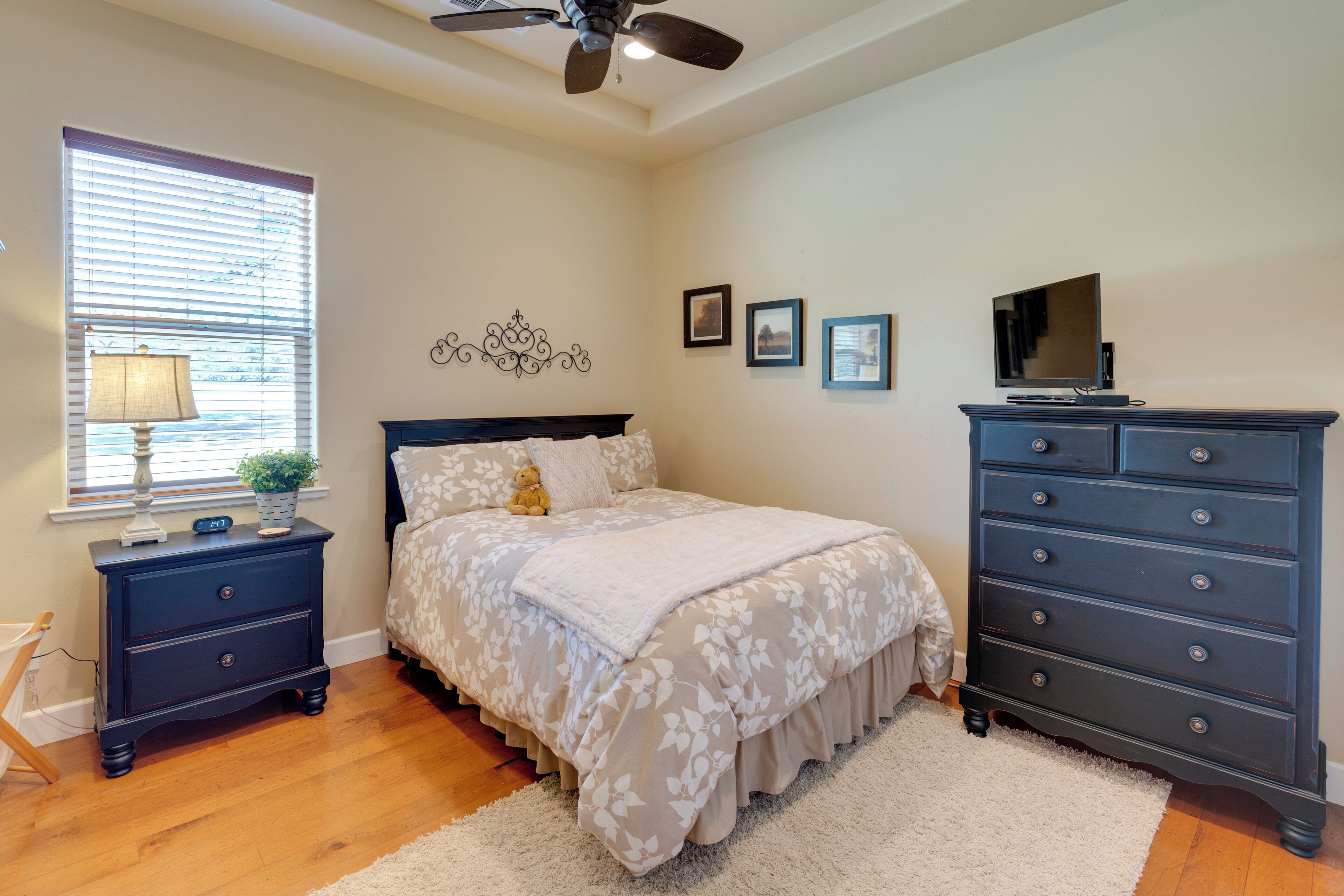 A bedroom with a bed, nightstand, dresser, TV, and decorative wall art.