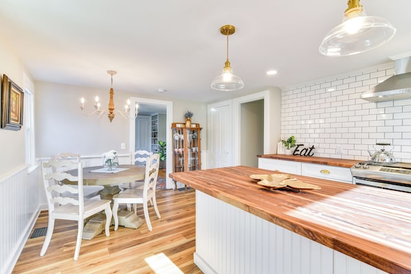 Une cuisine avec un îlot central en bois, des meubles blancs et un mur de fond en briques.