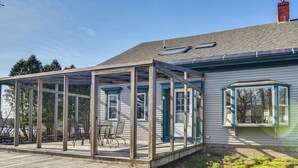 A house with a covered patio area, a visible chimney, and a window with a view of trees. - Quiet Waterfront Home: Ideal Maine Escape! (Bass Harbor)