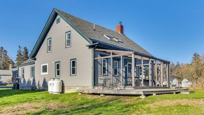 A two-story house with a covered porch and a large water tank in the yard. - Quiet Waterfront Home: Ideal Maine Escape! (Bass Harbor)