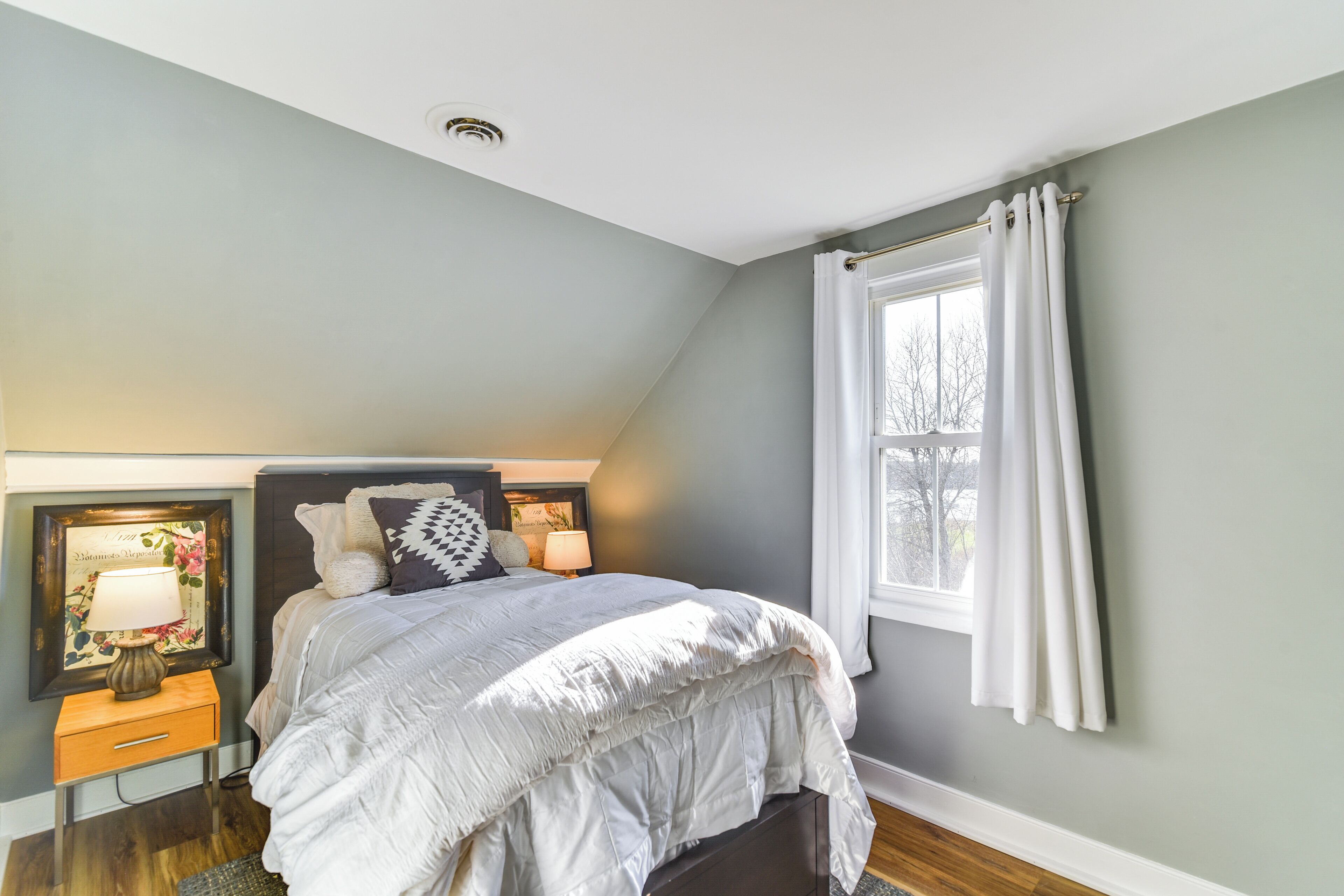Un dormitorio con cama, mesita de noche, lámpara y ventana con cortinas.