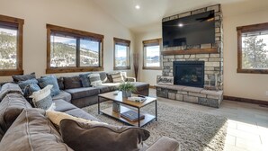 A spacious living room with a stone fireplace, large windows, and a cozy sectional sofa. - ~ 3 Mi to Granby Ranch: Spacious Cabin Home! (Granby)