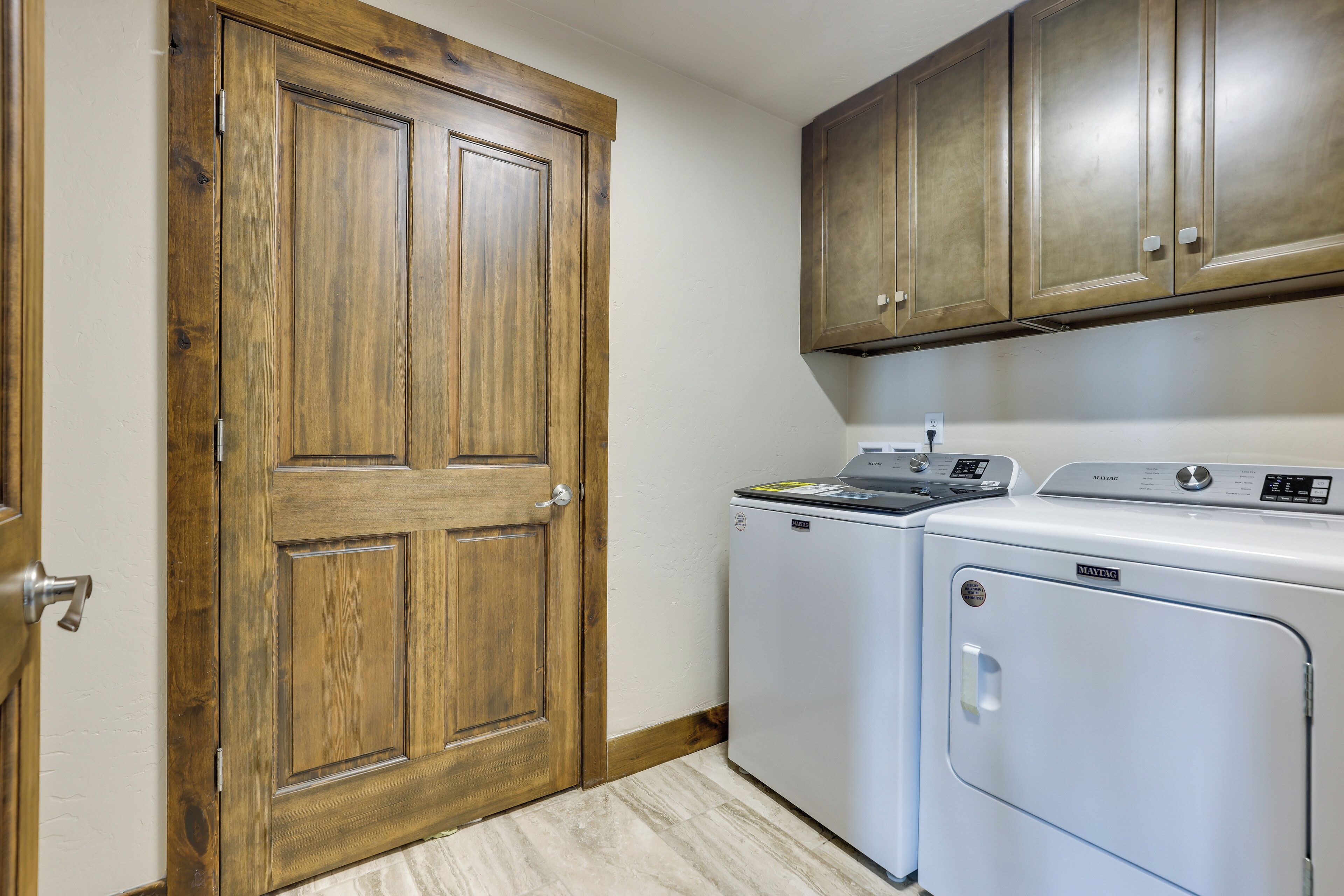 A laundry room with a wooden door, a washing machine, and cabinets above.