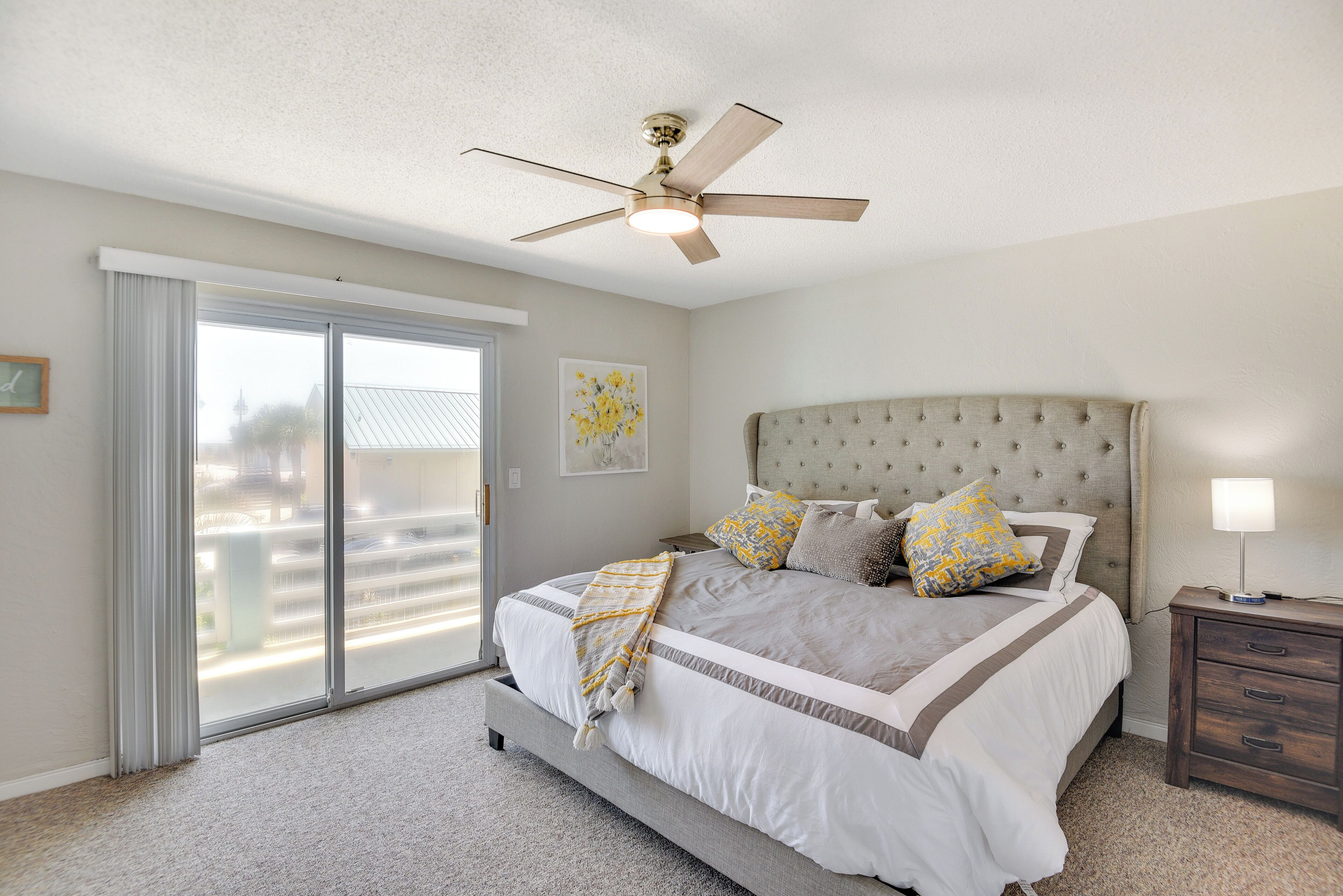 A bedroom with a large bed, a ceiling fan, a sliding glass door, and a nightstand with a lamp.