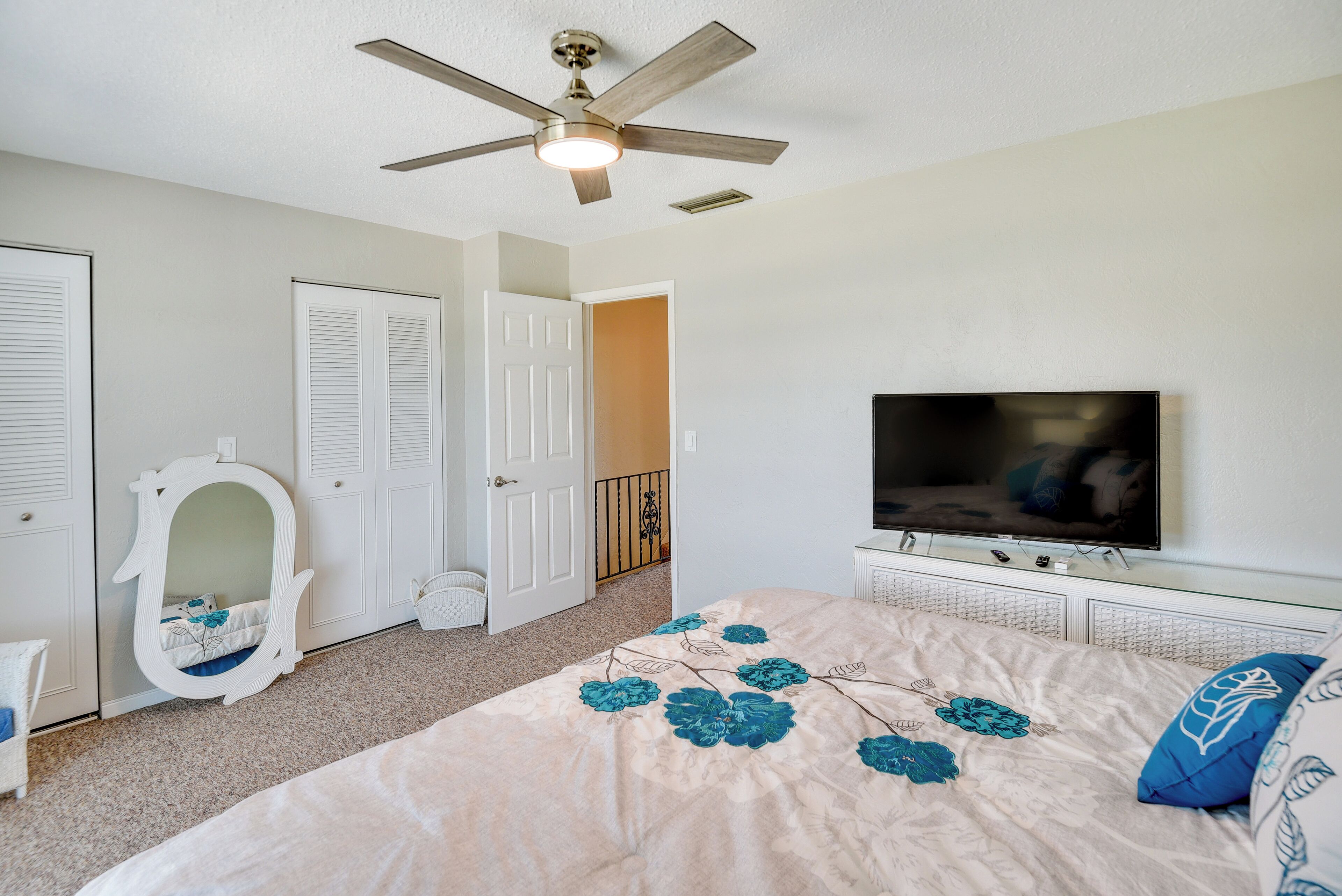 Un dormitorio con cama, ventilador de techo, televisor y puerta.