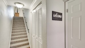 Eine Treppe mit einem 'welcome'-Schild, weißen Türen und einer Lampe.