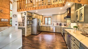 Une cuisine spacieuse agrémentée d’éléments en bois, d’un pare-feu en pierre et d’un plafond haut avec des poutres apparentes.