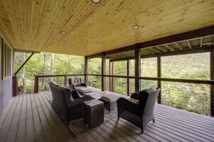 Un espacio de estar al aire libre cubierto, con mobiliario de mimbre y vistas a un paisaje boscoso.