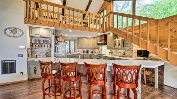 Une cuisine spacieuse avec un grand îlot central, un escalier en bois et une vue sur la verdure environnante.