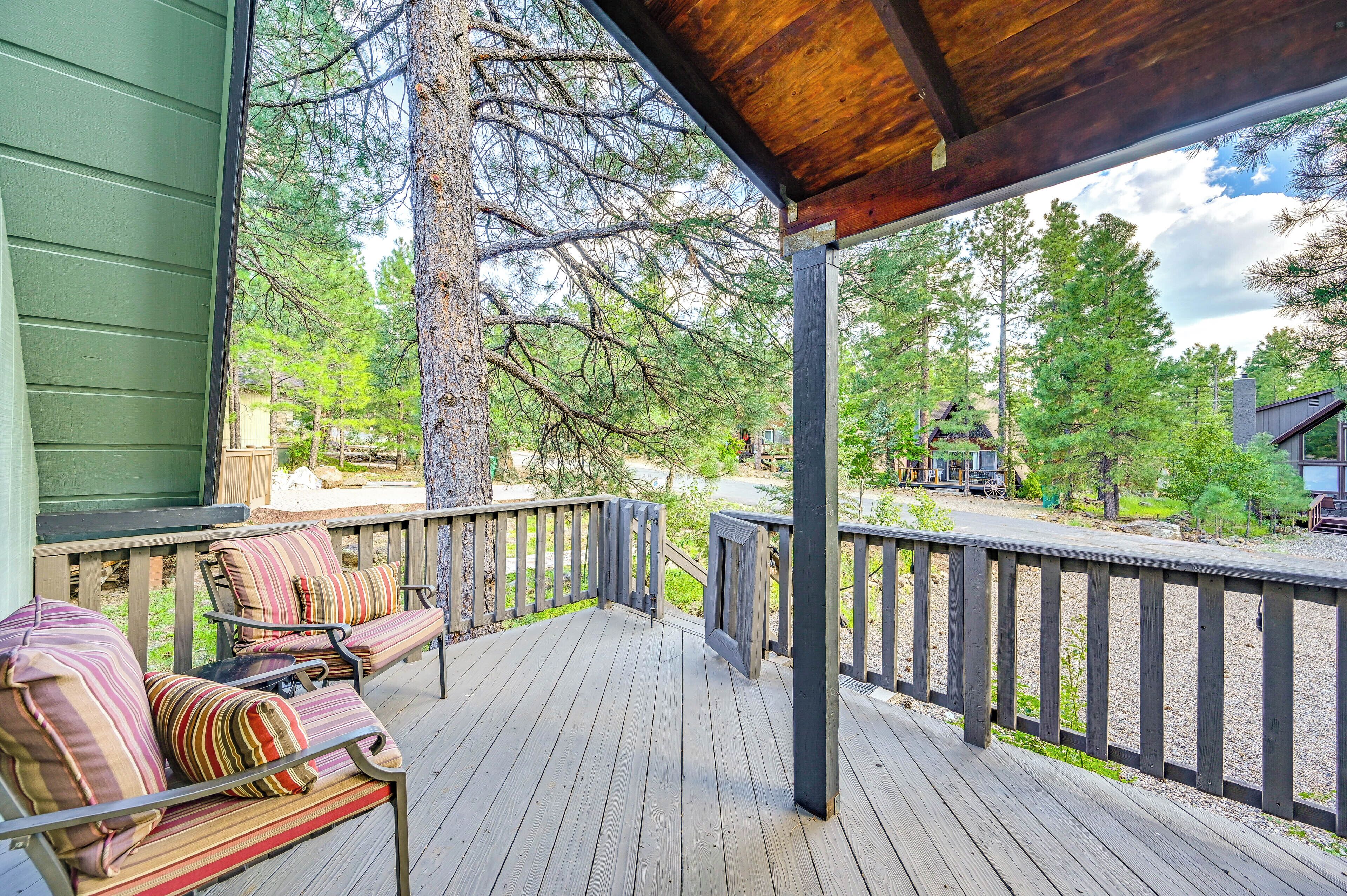A wooden deck with a covered area, outdoor seating with striped cushions, and a view of a forested area.