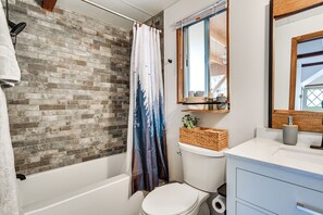 Une salle de bain avec un mur en briques, un rideau de douche, des toilettes, un lavabo et un miroir.