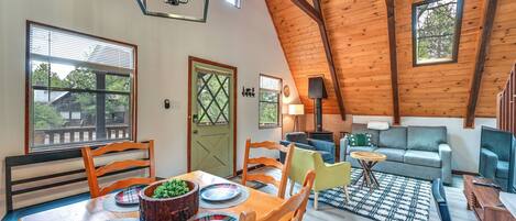 A spacious loft-style living area with a high ceiling, wooden beams, and large windows offering views of the outdoors.