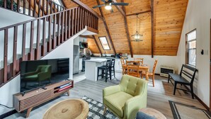 A spacious loft with a high ceiling, wooden beams, a kitchen area, a dining space, and a living area with a television and seating. - Deck & Grill: A-frame Cabin in Munds Park! (Munds Park)