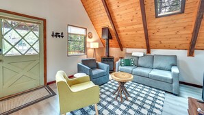 A cozy room with a sloped ceiling, a fireplace, a sofa, a chair, and a small table. - Deck & Grill: A-frame Cabin in Munds Park! (Munds Park)