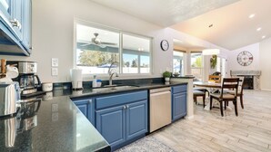 A modern kitchen with blue cabinets, a dishwasher, and a dining area with a table and chairs. - Pool, Putting Green & Games: Chandler Home! (Chandler)