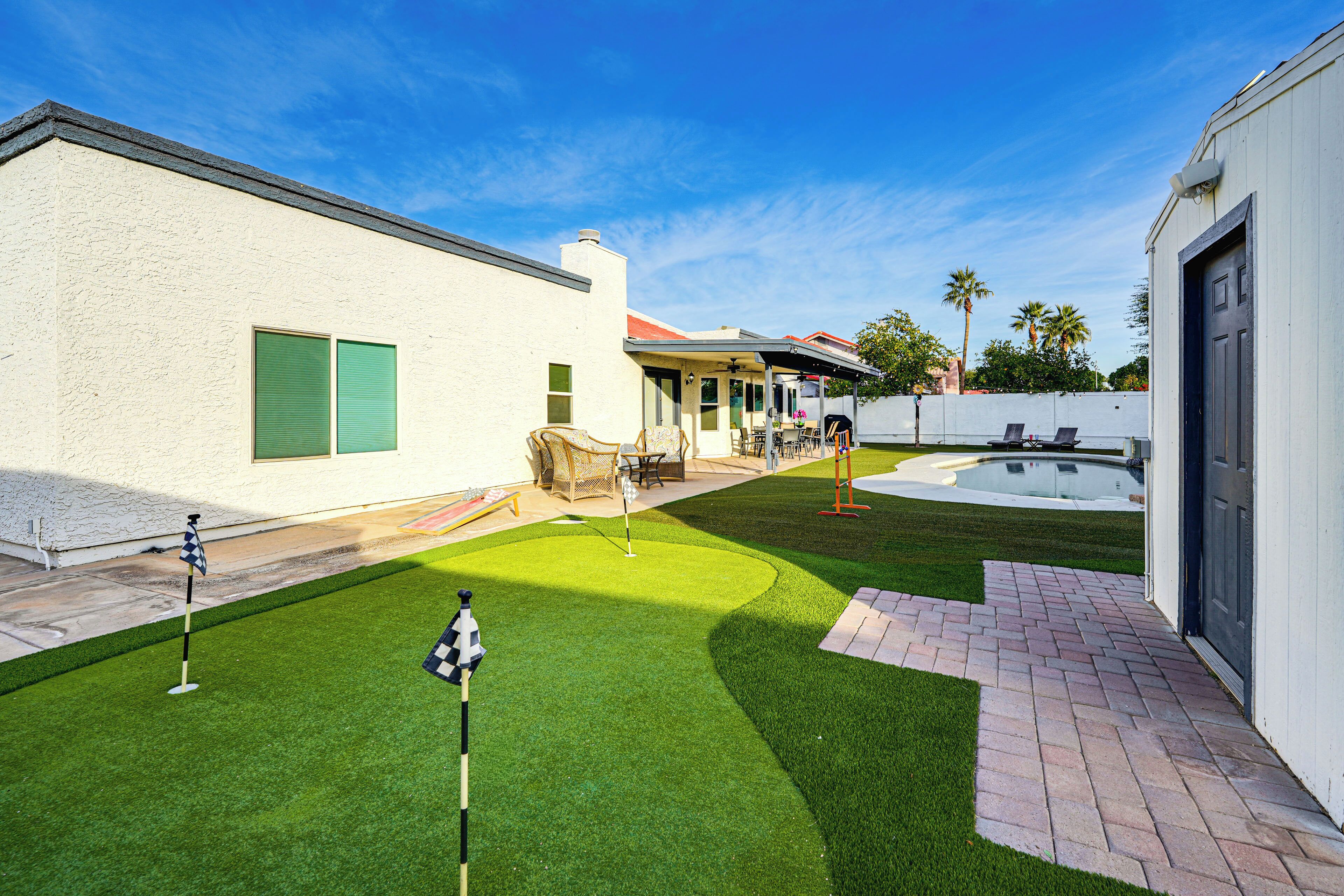 A backyard with artificial grass, a pool, and a patio area.