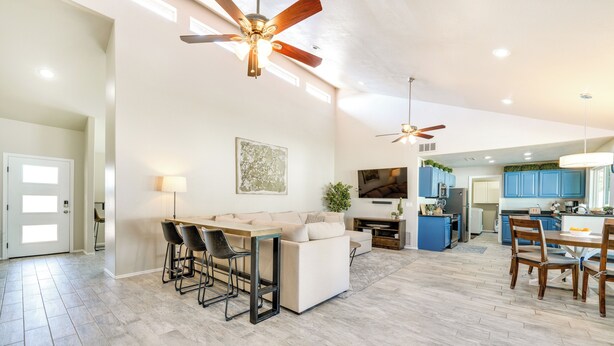 A spacious living area with a sofa, dining table, and chairs, a kitchen with blue cabinets, and ceiling fans. - Pool, Putting Green & Games: Chandler Home! (Chandler)