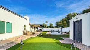 A backyard with artificial grass, a pool, and a patio area with outdoor furniture. - Pool, Putting Green & Games: Chandler Home! (Chandler)