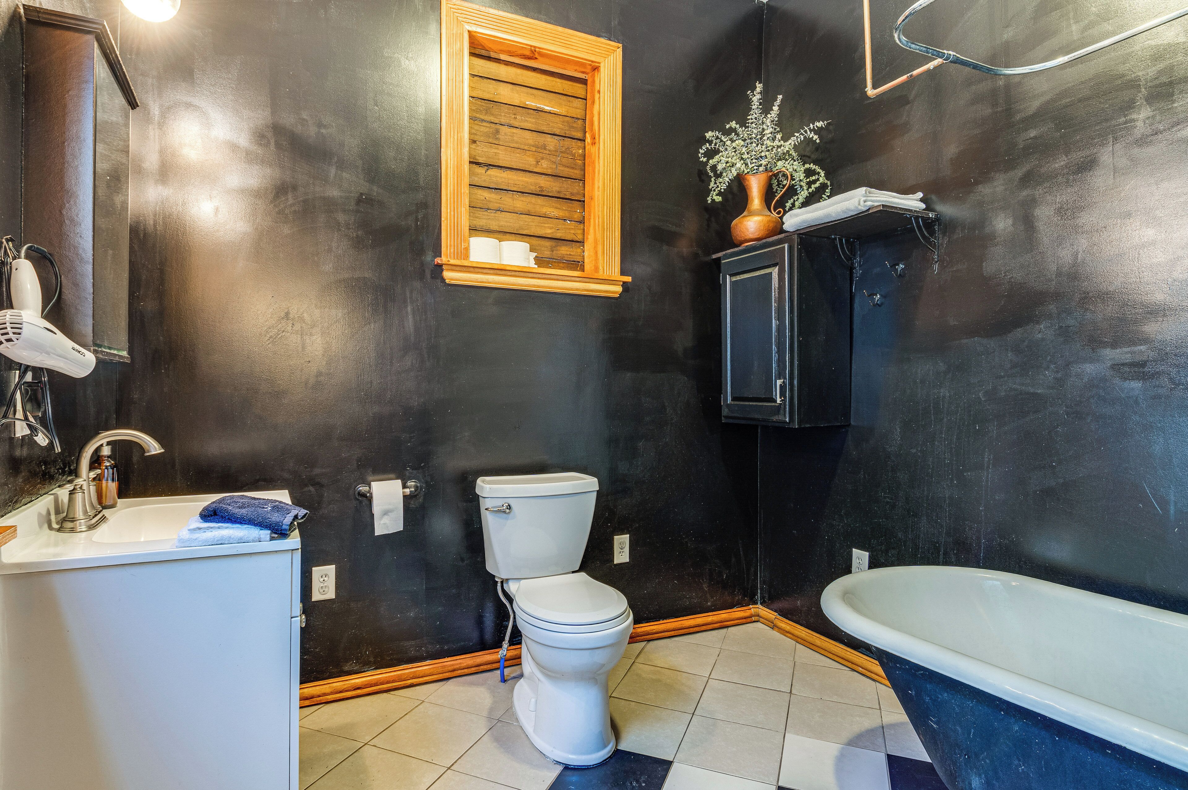 A bathroom with a black wall, a wooden-framed window, a white toilet, a white sink, and a blue bathtub.