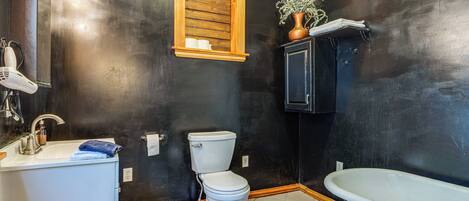 A bathroom with a black wall, a wooden-framed window, a white toilet, a white sink, and a blue bathtub.