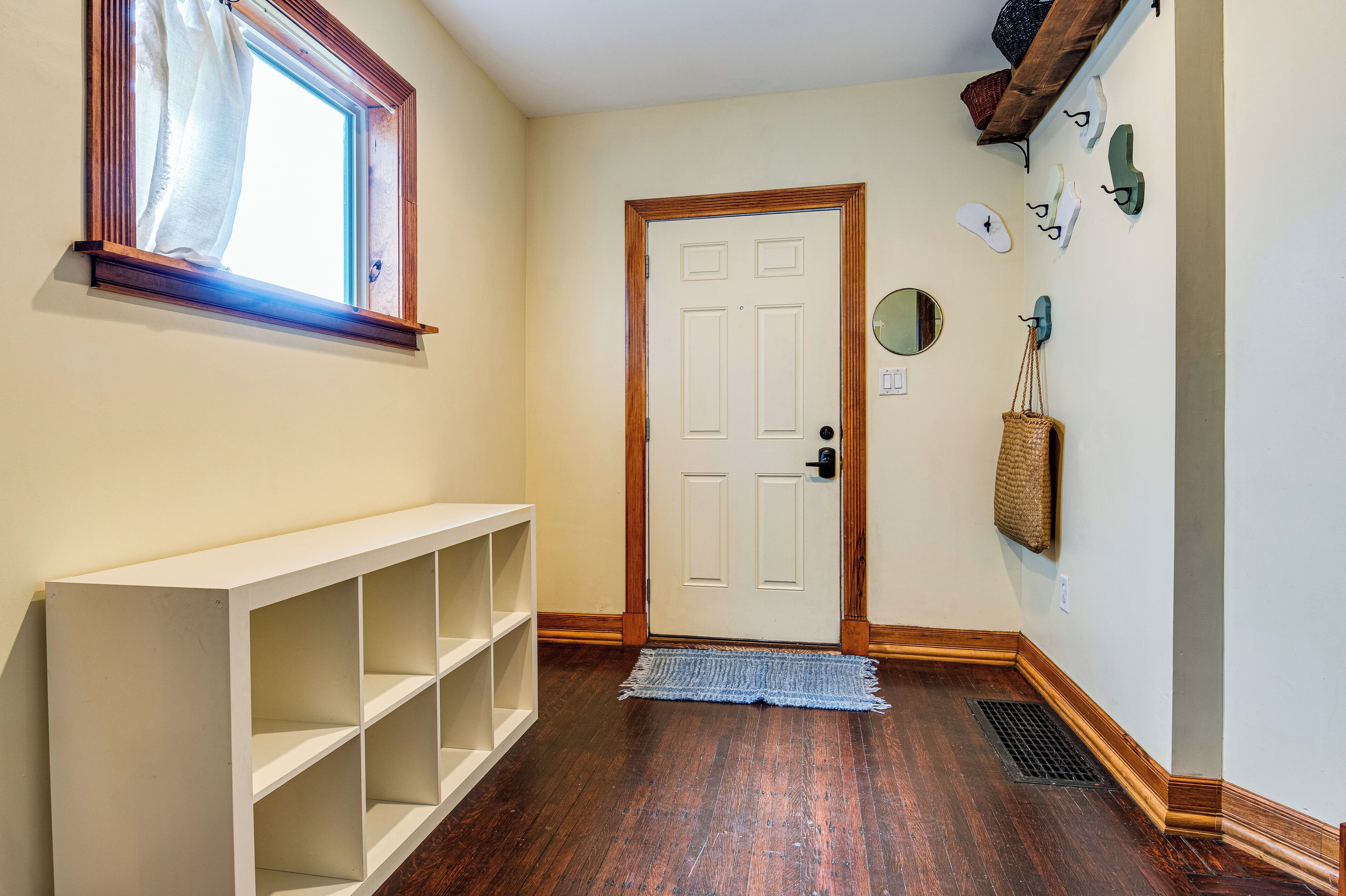A hallway with a white console table, a wooden floor, a white door, and a window with a wooden frame.