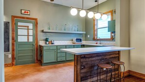 A kitchen with green cabinets, a white countertop, and a wooden island with stools. There is a microwave, a coffee maker, and a window with blinds. - Cozy Indianapolis Vacation Rental w/ Micro Farm! (Indianapolis)