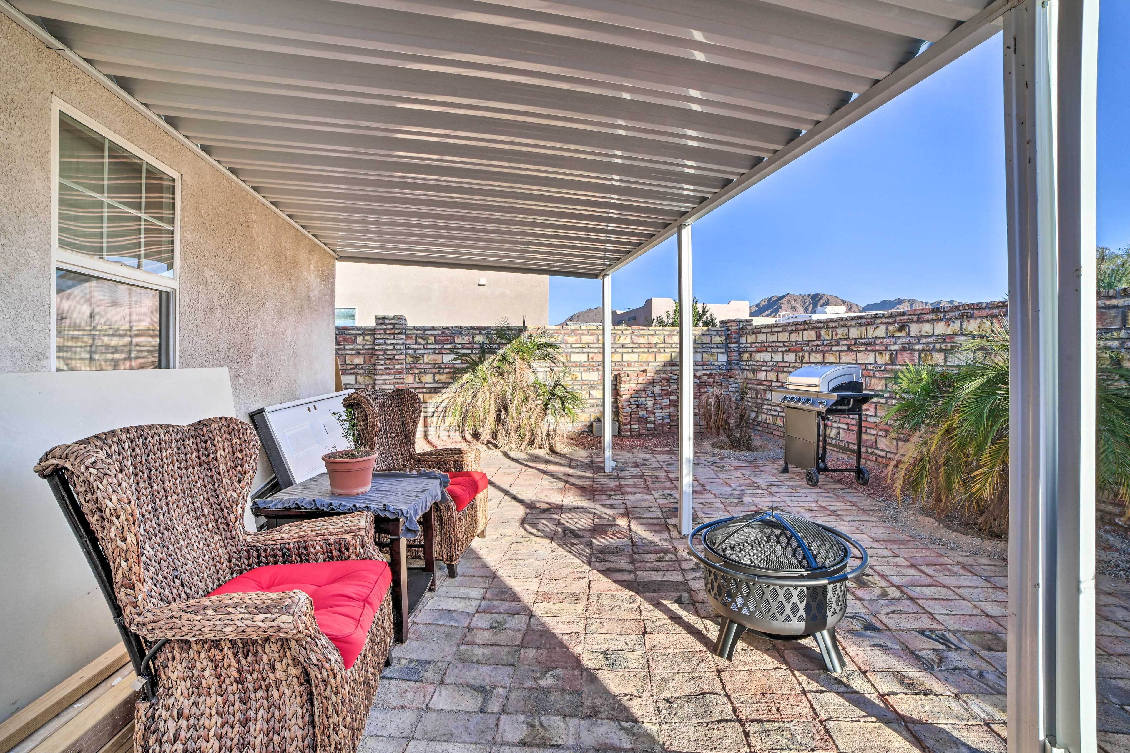Une terrasse couverte, aménagée avec des meubles en osier, un barbecue et offrant une vue sur les montagnes.
