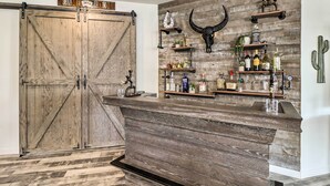 A rustic bar area with a wooden counter, shelves with bottles, and a large wooden door. - Private Pool: Stunning Goodyear Vacation Rental! (Goodyear)