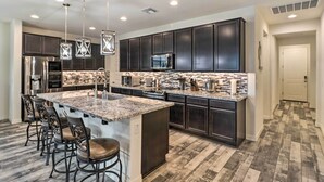 A modern kitchen with dark cabinets, a granite countertop, and a central island with bar stools. - Private Pool: Stunning Goodyear Vacation Rental! (Goodyear)