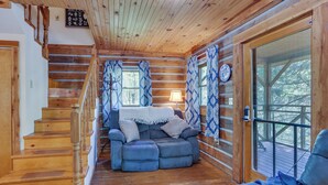 Ein Holzblockhaus-Innenraum mit einer Holztreppe, einem blauen Sofa und einer Glastür, die nach draußen führt.